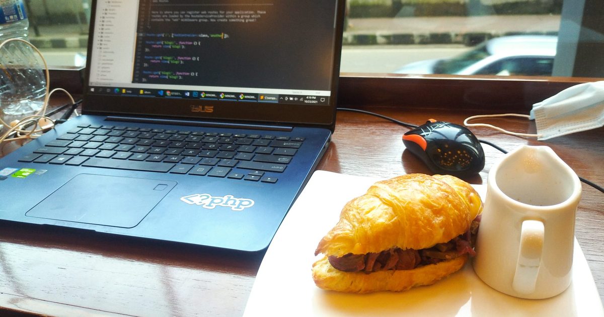 Laptop showing code on a coffee shop table next to a sandwich and coffee